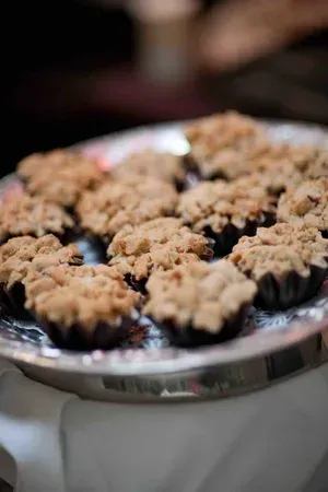 Tray of small crumb-topped desserts on a round silver platter, slightly out of focus