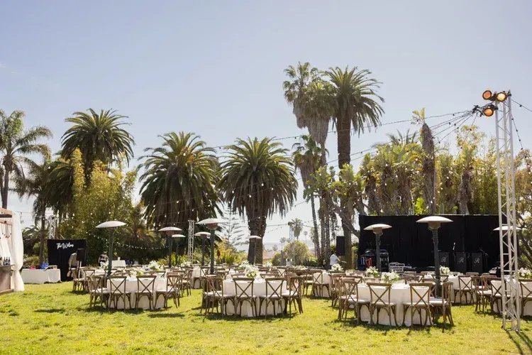 Outdoor café seating on a sunny lawn with palm trees and string lights in the background