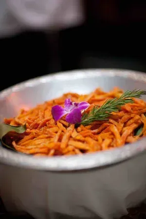Metal bowl of orange pasta topped with herbs and a purple edible flower