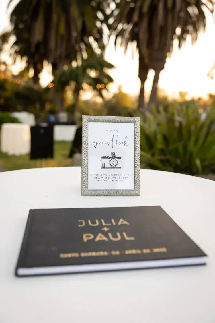 Wedding table card and framed sign on a white table outdoors with palm trees in the background