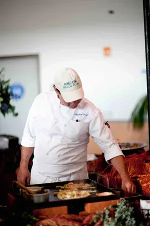 Chef in white uniform and cap preparing food at a buffet counter