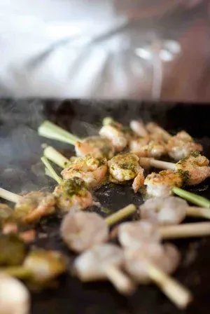 Skewered appetizers on a grill, with browned pieces and green garnish cooking over heat