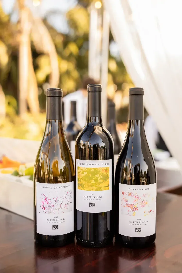 Three wine bottles with white and yellow labels on a table outdoors, against a blurred patio backdrop