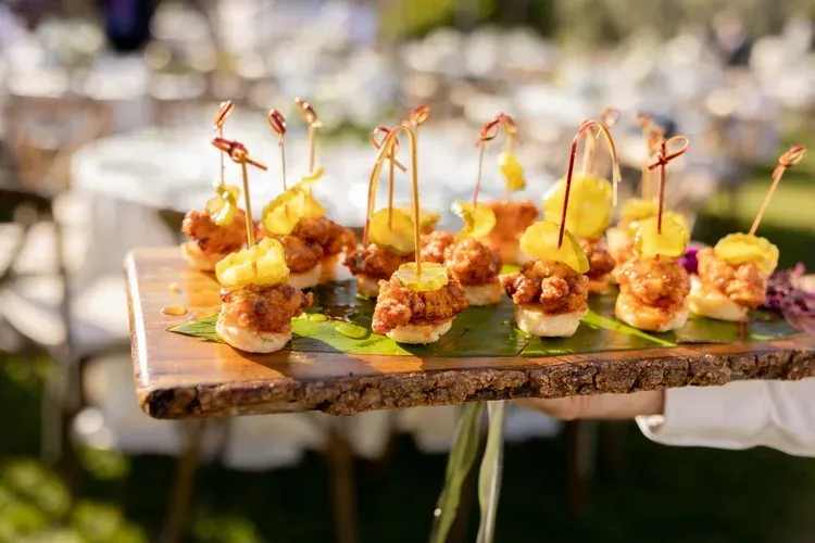 Tray of bite-sized appetizers with skewers on a rustic table outdoors at an event