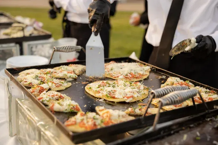 Flatbread pizzas cooking on a large griddle at an outdoor food buffet