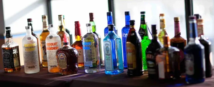 Assorted liquor bottles lined up on a bar counter, with colorful glass and labels.