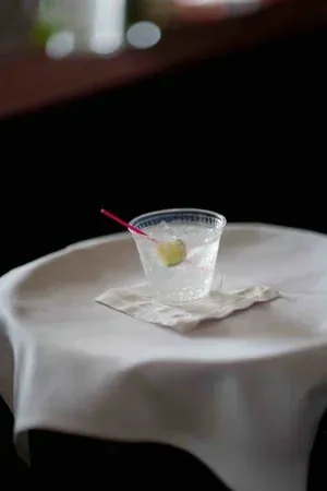 A clear plastic cup with a red straw and lemon wedge on a white tablecloth, against a dark background