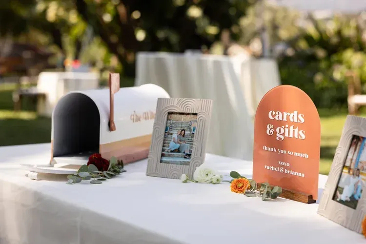 Wedding welcome table with framed signs, flowers, and cards on a white tablecloth outdoors