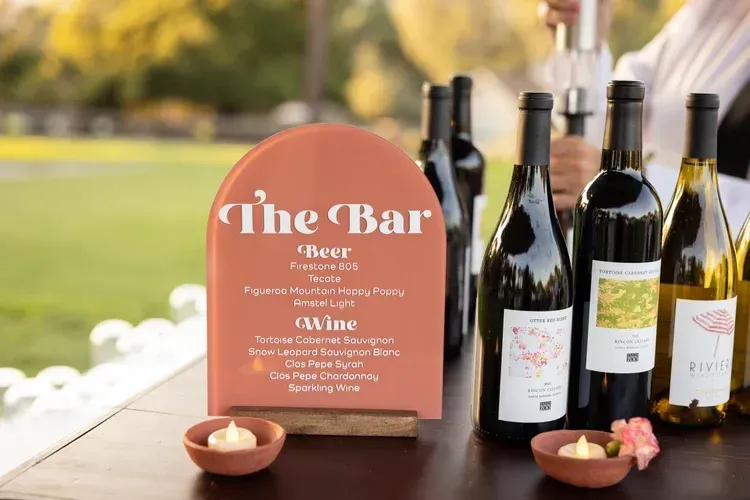 Rustic wine bar sign with bottles and candles on a table outdoors