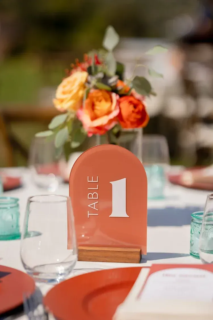 Orange floral table number card on a set dining table with glassware and plates