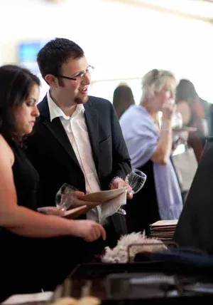 People chatting at a networking event, with a man in a black suit holding a drink and plate.
