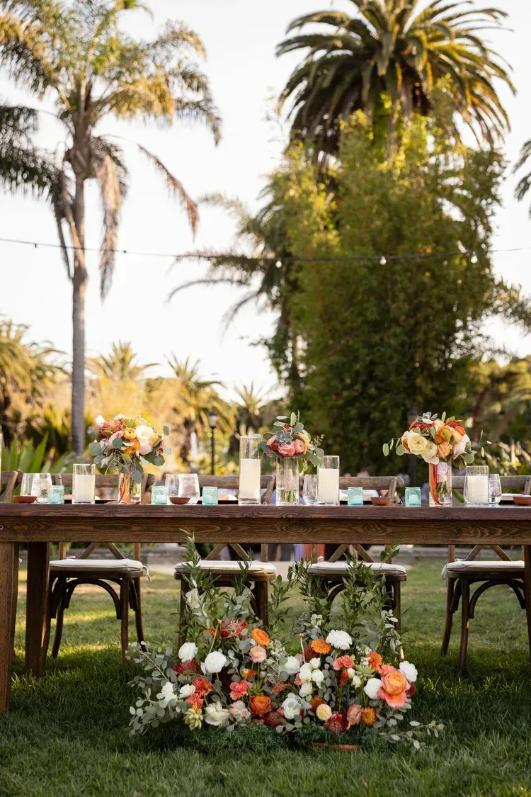Outdoor wedding reception table decorated with flowers, set on a lawn with palm trees in the background