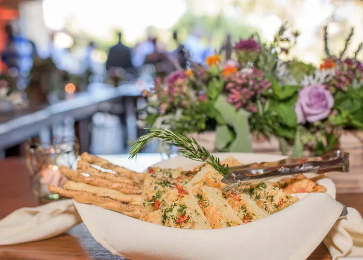 Plated breadsticks with herbs and dip on a table, with a blurred floral restaurant setting behind.