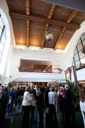 Crowded indoor gathering in a bright hall with a wooden vaulted ceiling and balcony