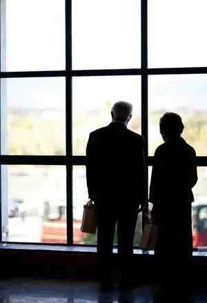 Two silhouetted people standing by a large window in a bright building lobby