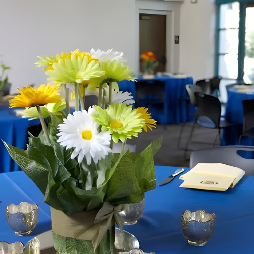 Bouquet of white and yellow flowers in a vase on a blue-covered table in a meeting room.