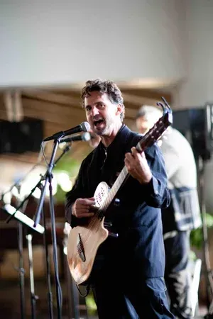 Musician singing into a microphone while playing a small stringed instrument on stage