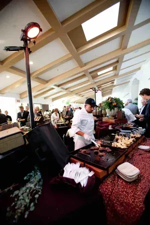 Buffet table with people serving food under a bright skylit ceiling