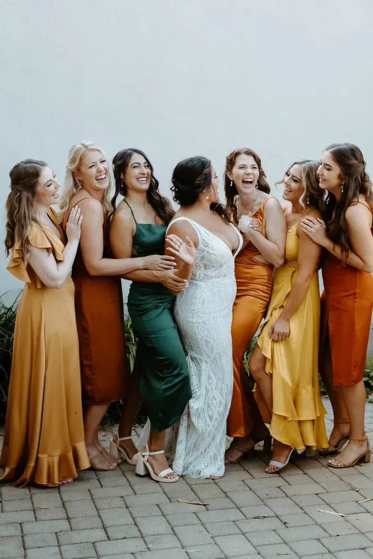 Group in elegant formal dresses smiling outdoors on a paved walkway.