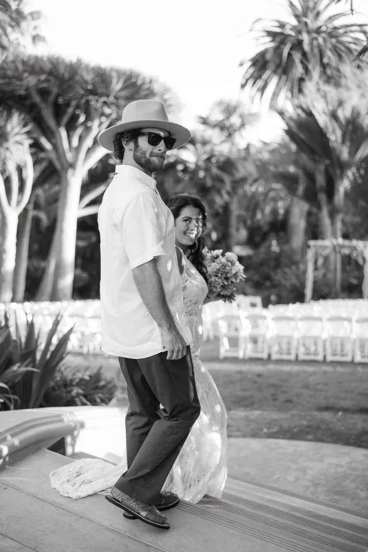 Couple dancing outdoors in a tropical garden, with palm trees in the background.