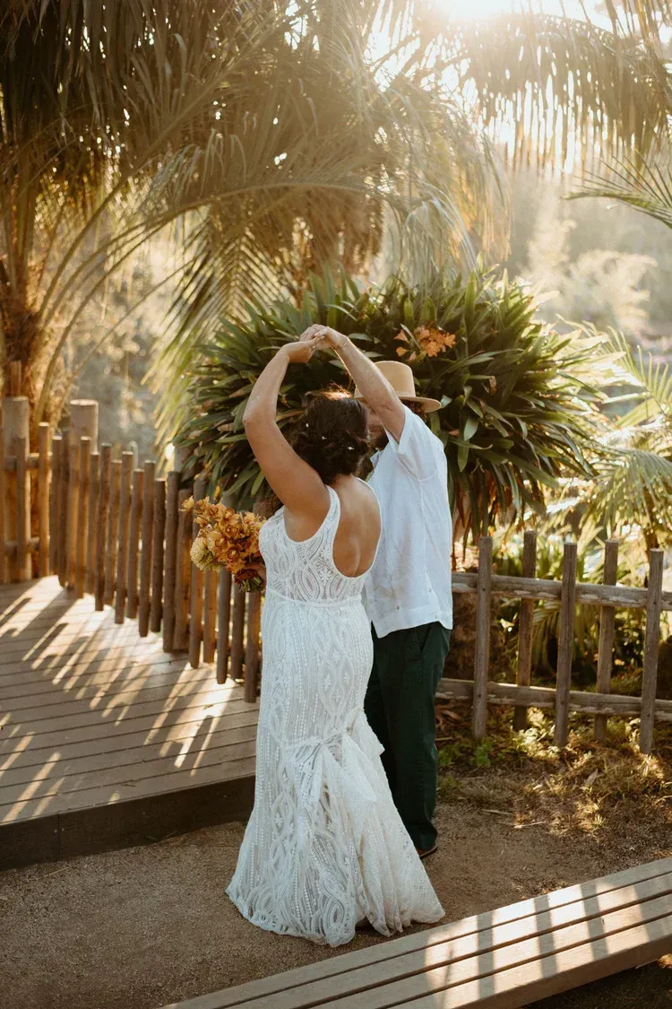 Couple dancing under palm trees on a sunlit wooden deck, with warm golden light filtering through the leaves
