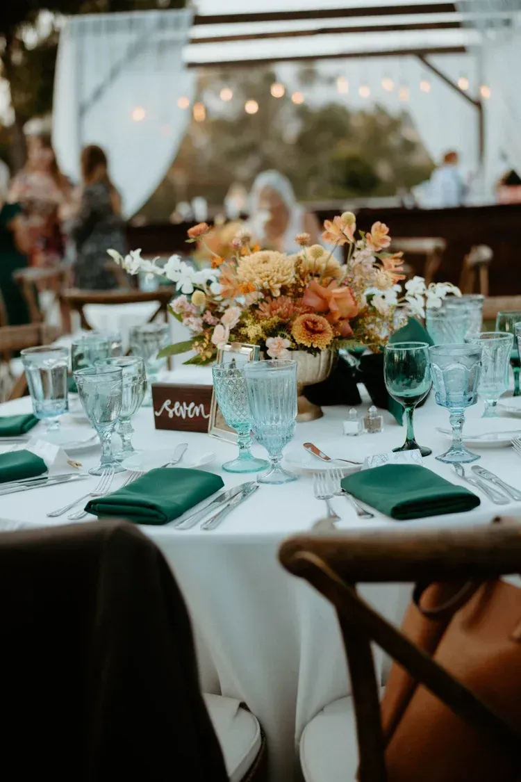 Elegant outdoor wedding reception table with flowers, green napkins, glassware, and warm string lights