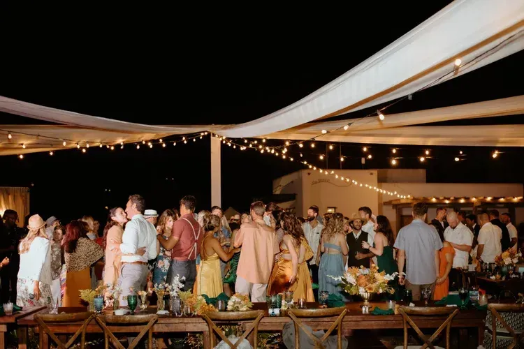 Guests mingling at an outdoor evening reception under white draped canopies and string lights