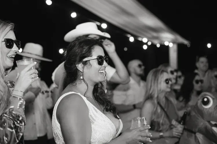 Crowd dancing at a nighttime outdoor party, with guests holding drinks under string lights.