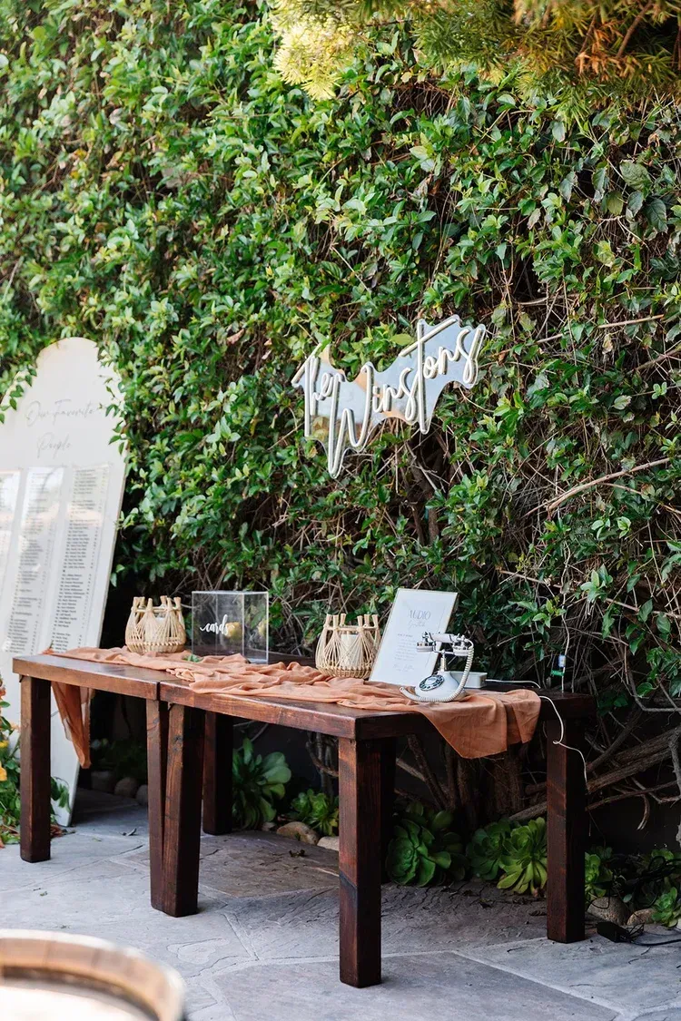 Wooden display table against a green ivy wall with framed prints and a hanging sign