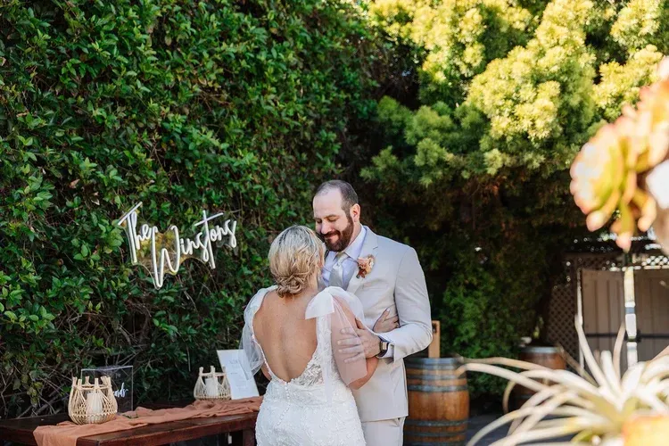 Bride and groom embracing in a sunlit garden wedding ceremony near a greenery wall