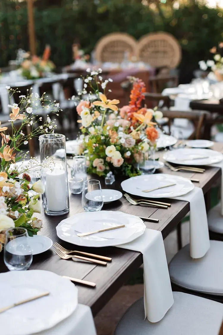 Elegant outdoor dining table set with white plates, candles, and colorful floral centerpieces