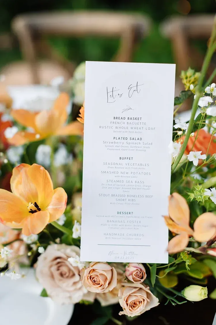 White wedding menu card amid peach and cream flowers on a floral arrangement display
