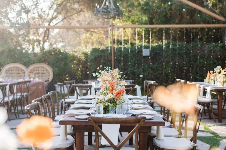 Outdoor dining table set with white chairs and floral centerpiece in a sunlit garden patio