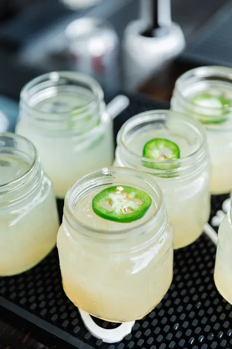 Small mason jars of pale yellow drinks topped with lime slices on a tray