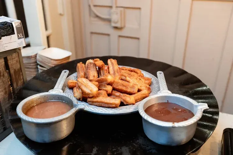 Two metal bowls of curry with a plate of fried snacks on a black table
