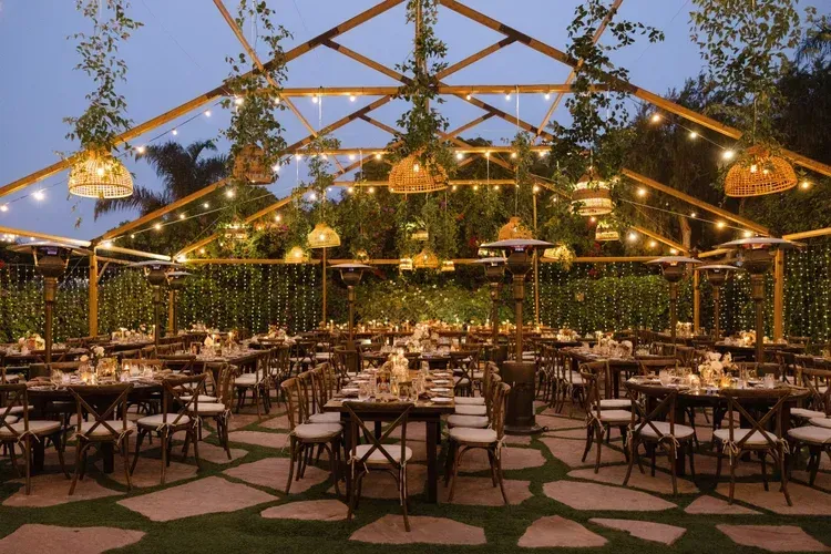 Elegant outdoor dining tent with string lights, set tables, and lush greenery at dusk