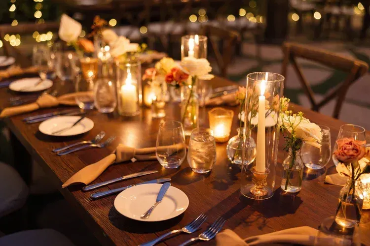 Candlelit outdoor dining table set with plates, glasses, flowers, and warm string lights at dusk
