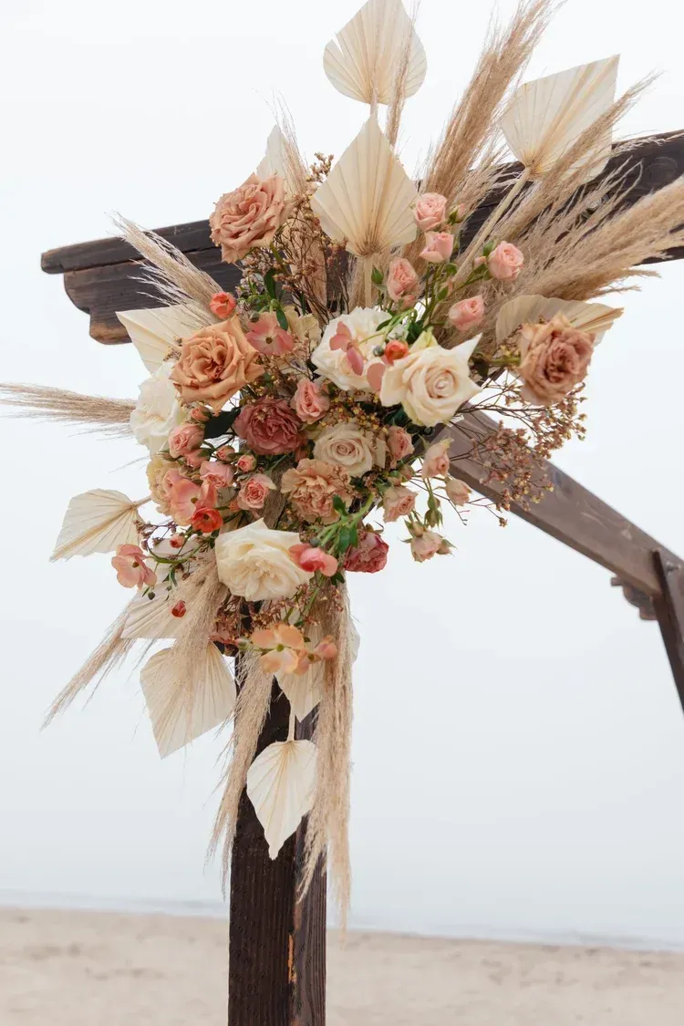 Floral arrangement with beige and peach flowers on a wooden arch outdoors
