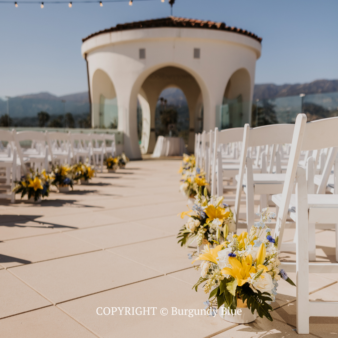 Decorated outdoor wedding aisle with white chairs and a beige pavilion under a clear sky