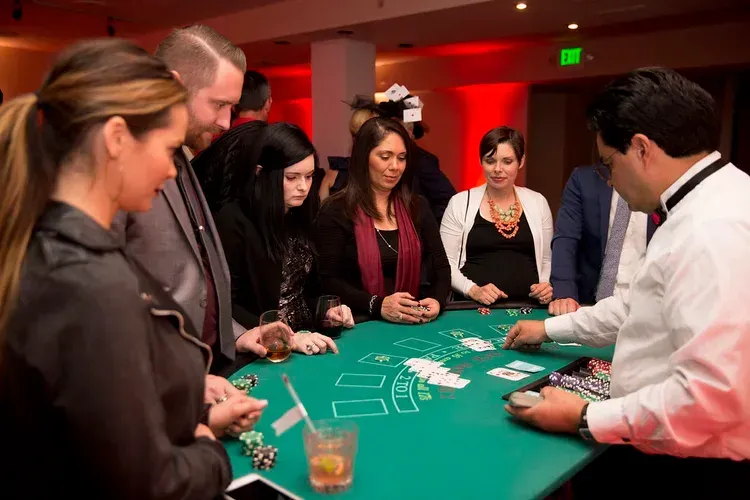 People gathered around a green casino table, playing cards in a dimly lit room.