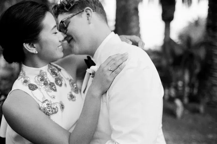 Couple in wedding attire embracing and kissing outdoors, with a blurred garden background