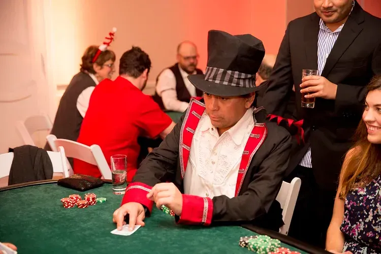 Man in a black top hat playing poker at a green table, with chips and other players nearby