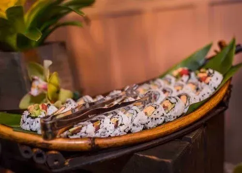 Sushi rolls on a wooden boat platter, garnished with lemon and flowers on a warm restaurant table
