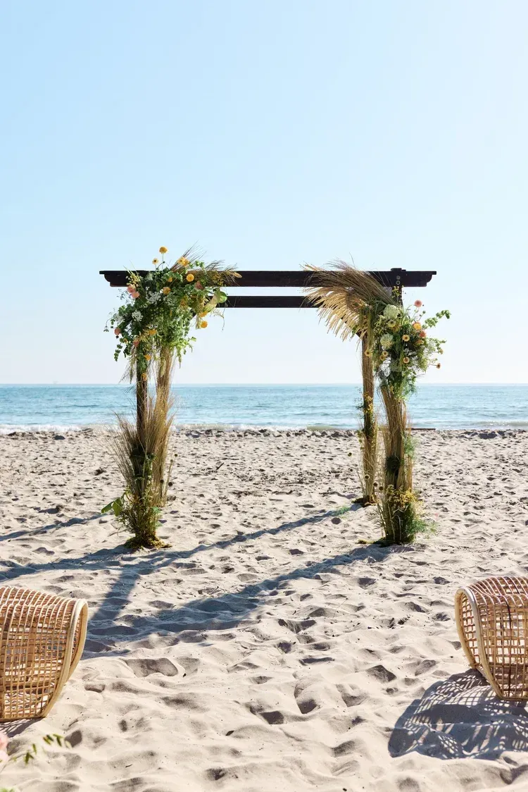 Beach wedding arch with greenery on a sandy shore by the ocean