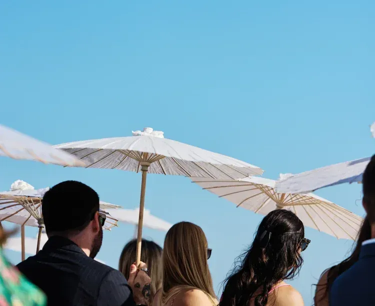 People holding white parasols under a clear blue sky