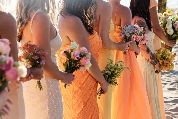 Bridesmaids in peach and cream dresses holding colorful bouquets at an outdoor wedding ceremony