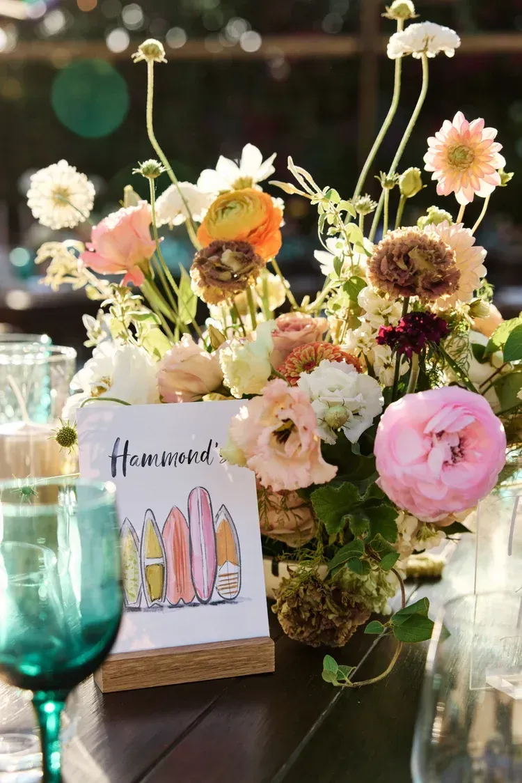 Floral centerpiece with pastel blooms and a small illustrated card on a table with glassware