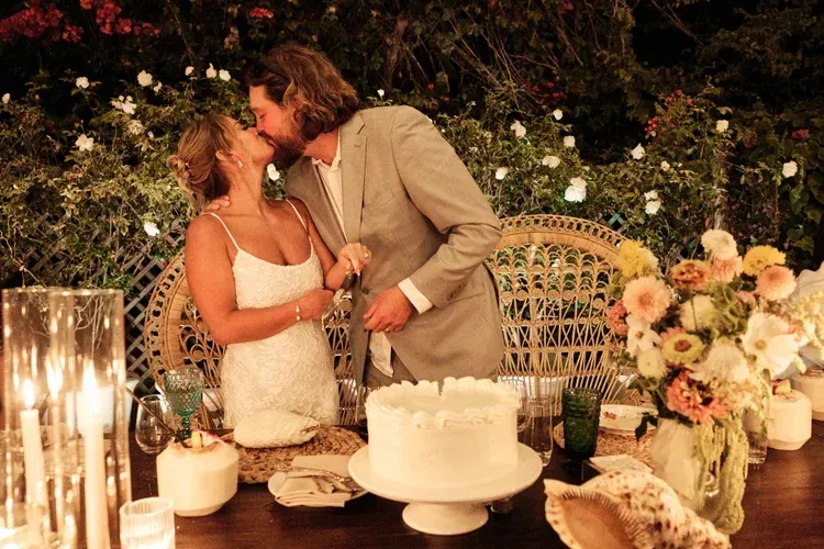 Couple kissing beside a decorated cake at an outdoor candlelit celebration