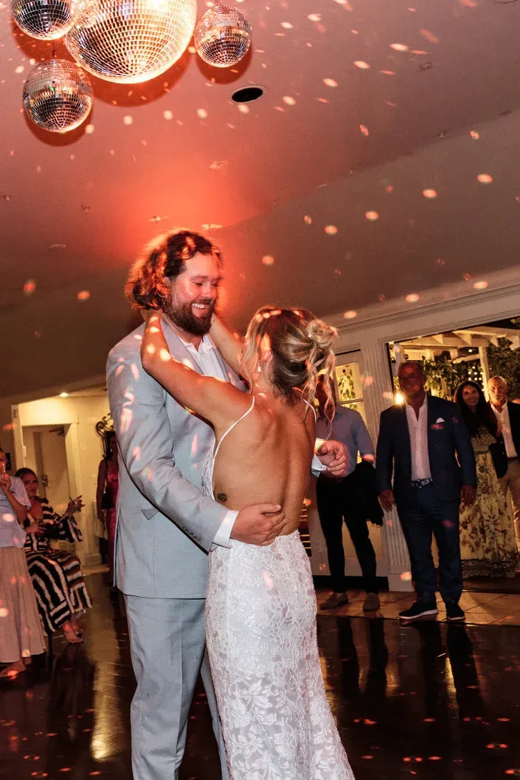 Couple slow dancing at a formal reception under warm pink lighting and disco balls