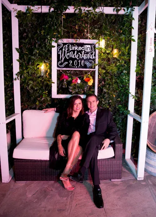 Couple seated on a bench beneath a lit “LinkedIn Local” sign at an evening event